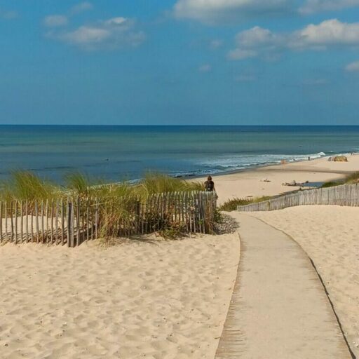 Beautiful pathway leading to a serene beach at Montalivet, under a vibrant blue sky.